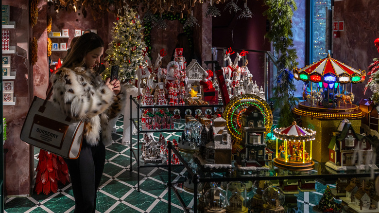 A young woman uses her mobile phone to take pictures of Christmas decorations on display for sale.