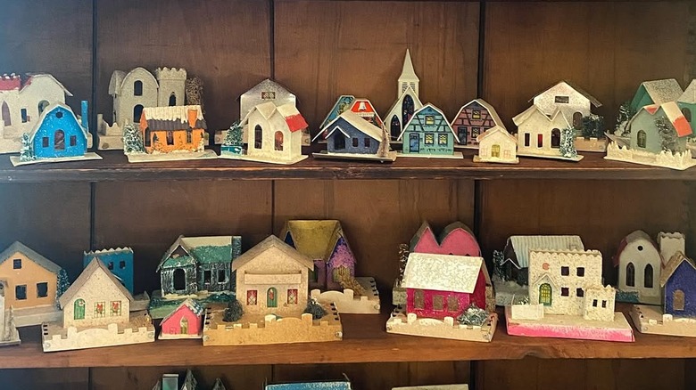 A display of vintage Christmas putz houses in wooden shelves.
