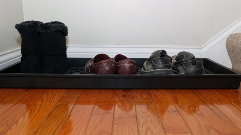 A black tray filled with shoes on a wood floor.
