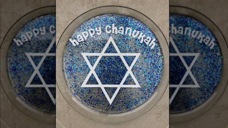 A clear drip tray decorated with blue glitter, a star of David, and the words "Happy Chanukah"