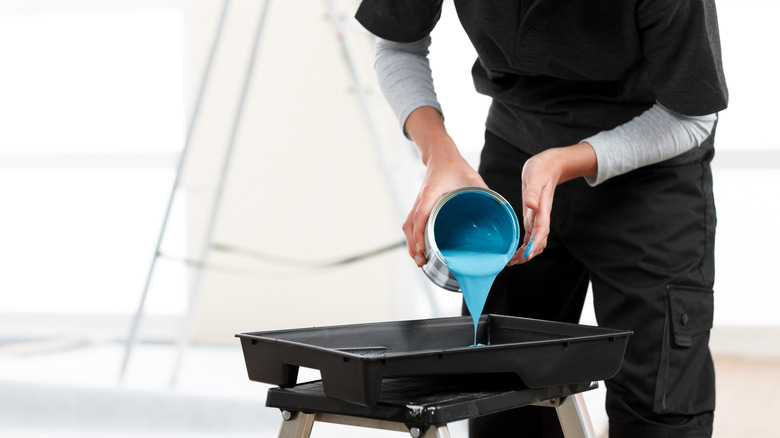 Someone pouring blue paint into a black tray.