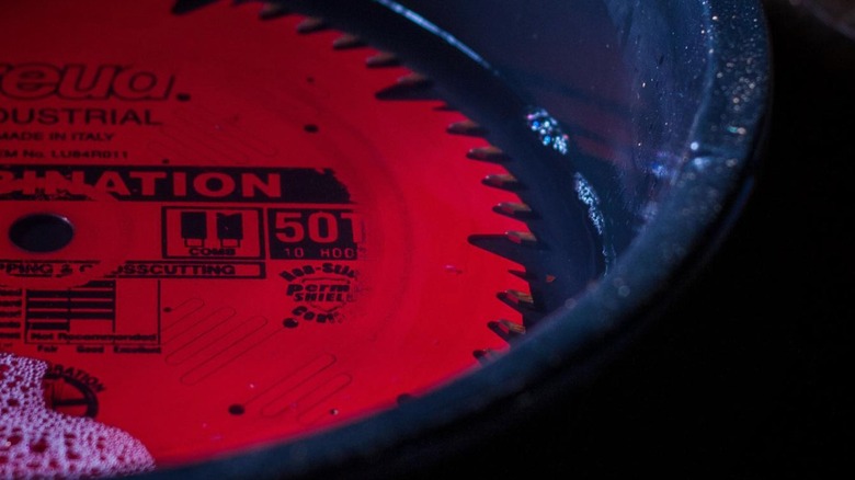 A black oil pan with water soaking a red saw blade.