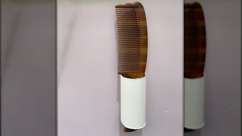 A brown comb hanging inside a toilet paper roll.
