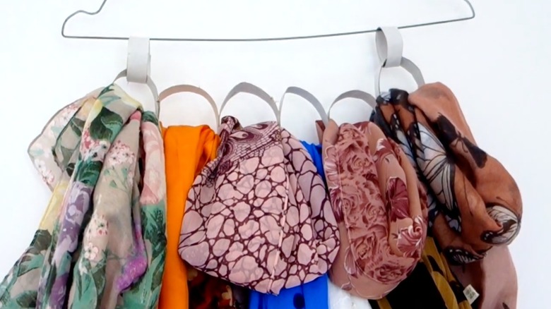 A hanger organizing scarves with toilet paper rolls.