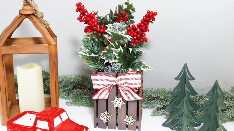 Mini pallet planter filled with winter berries and greenery with snowflakes on the front and a red and white bow