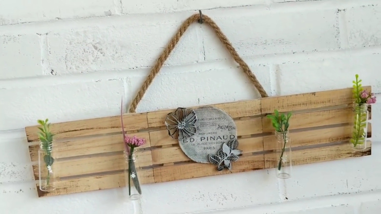 DIY sign made from three mini pallets displaying a floral theme and hanging on a white brick wall