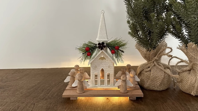 Mini pallet with lights underneath displaying a church and angels sitting next to two mini pine trees