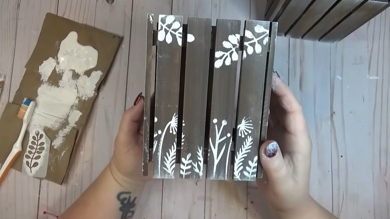 Creator holding the pallet lantern, which has a dark background and white leaf patterns on it