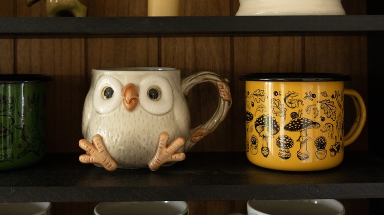 A funky owl mug and a yellow printed one on a shelf