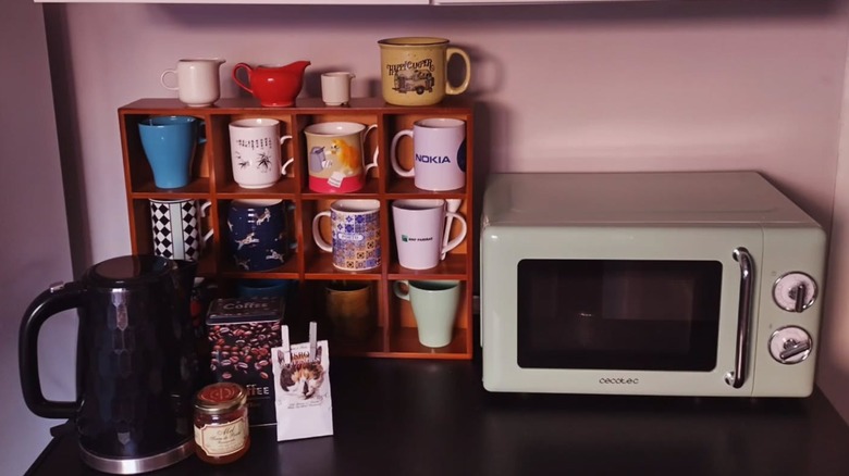 Coffee mugs on a small shelf on a countertop near oven and black kettle