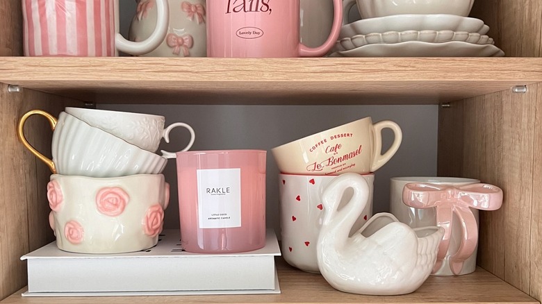 Mugs on a shelf with a decorative swan, candle, and book