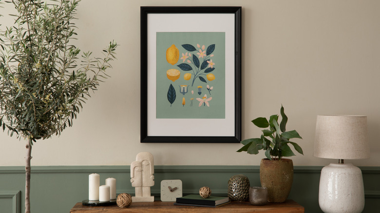 A sage-green artwork on the wall above an entryway console and next to an indoor olive tree.