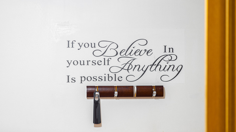 A stick-on vinyl motivating phrase on the wall above a row of coat hooks.
