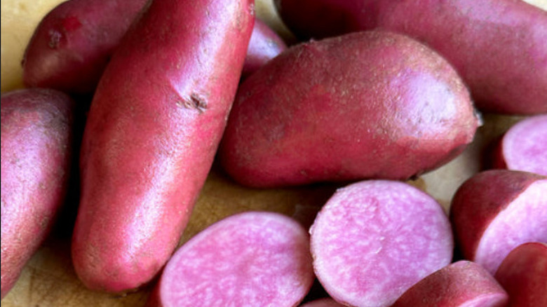 A pile of Ararosa Fingerling potatoes on a table with some cut into slices, showing off their pink and white marbled coloring
