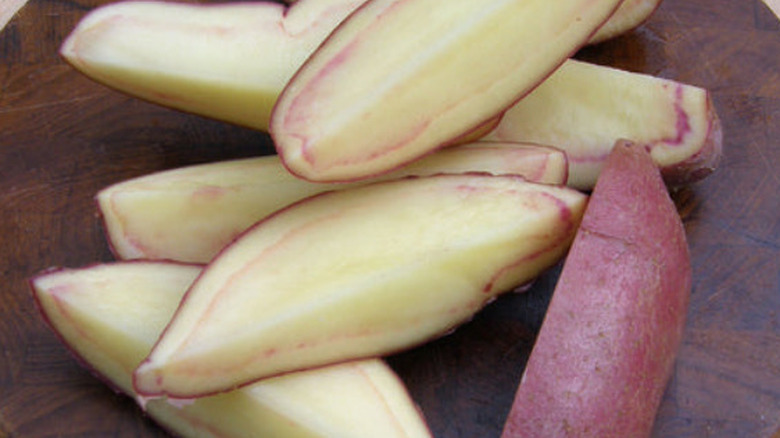 A close-up of quartered 'French Fingerling' potatoes on a wooden slab on a lighter wooden table