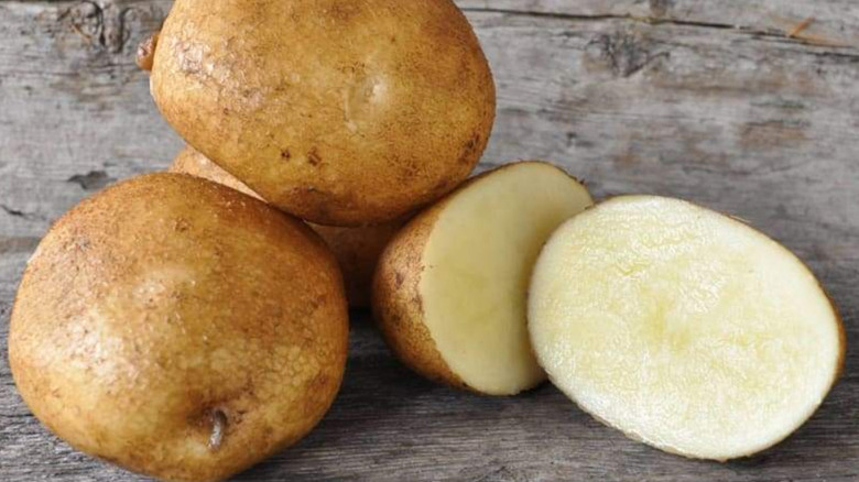 Several 'Keuka Gold' potatoes stacked on a rough wooden tables with one cut in half