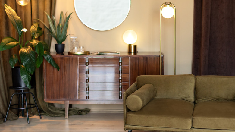 A living room with cabinet, couch, lighting, and plant.