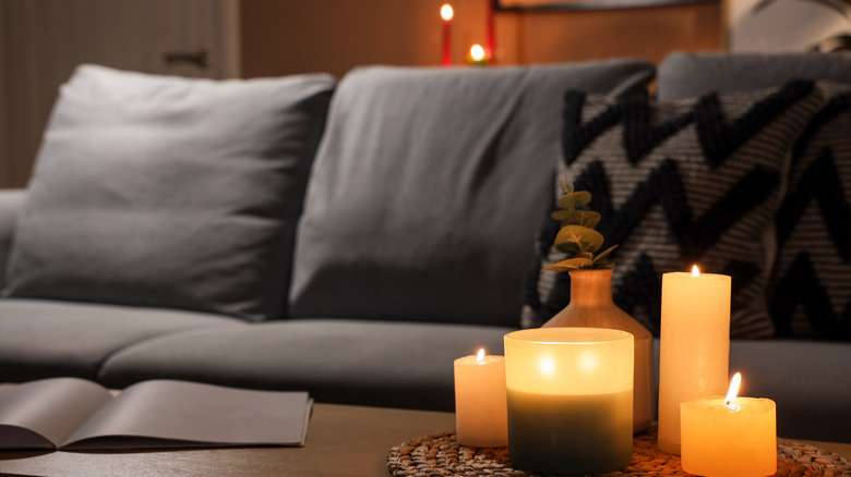 Six lit candles in a living room near a couch.