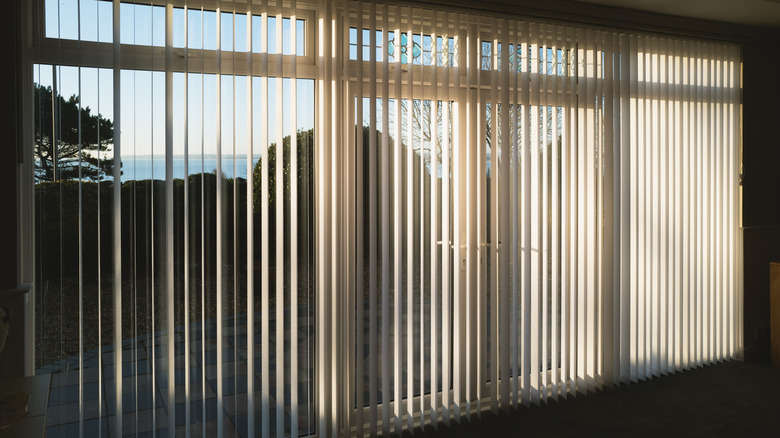 White vertical blinds that are open with sun shining through.