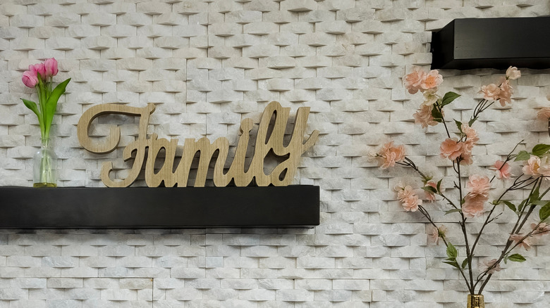A wood family sign on a shelf next to flowers.