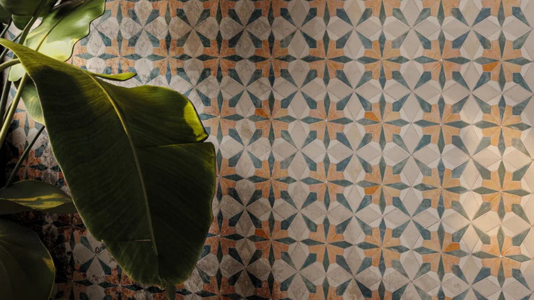 Floral tiles in black, two shades of beige and orange on a wall with a plant in the foreground