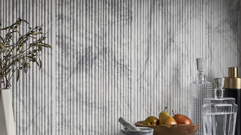 A series of vertical marble fluted tiles in a kitchen with several items like a bowl of fruit in front