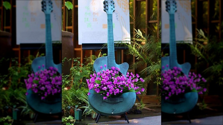 A blue guitar filled with growing flowering plants.