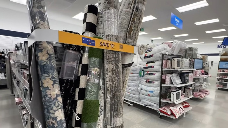 Rolled rugs (checkerboard, floral, solid green) on an endcap in a Ross store