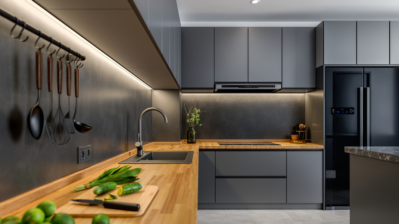 A kitchen with dark-colored cabinets and backsplash, as well as wood design counter.