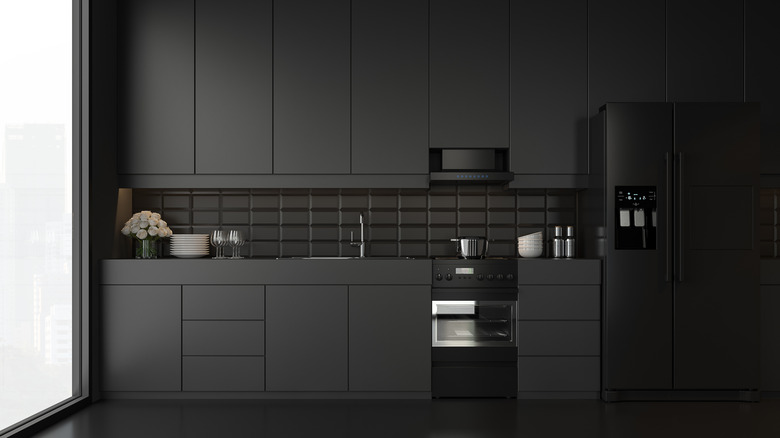 Matte-black kitchen cabinets, black refrigerator, stainless steel oven, and black subway tile backsplash with a wide glass window on one side.