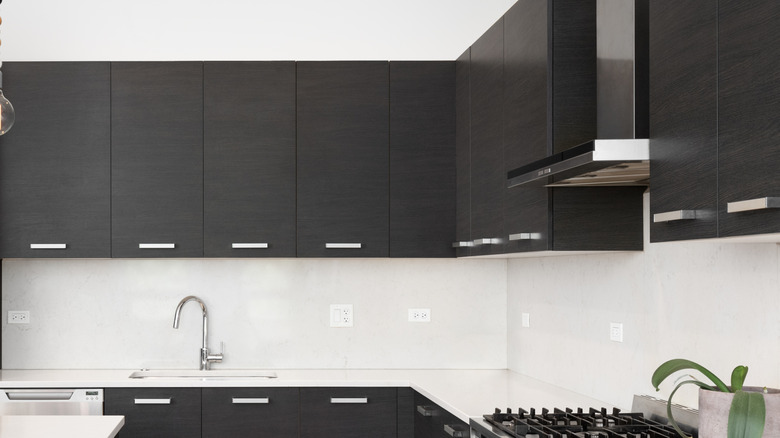 A beautiful kitchen with dark wood cabinets, marble countertops, chairs sitting at the island, and stainless steel appliances.