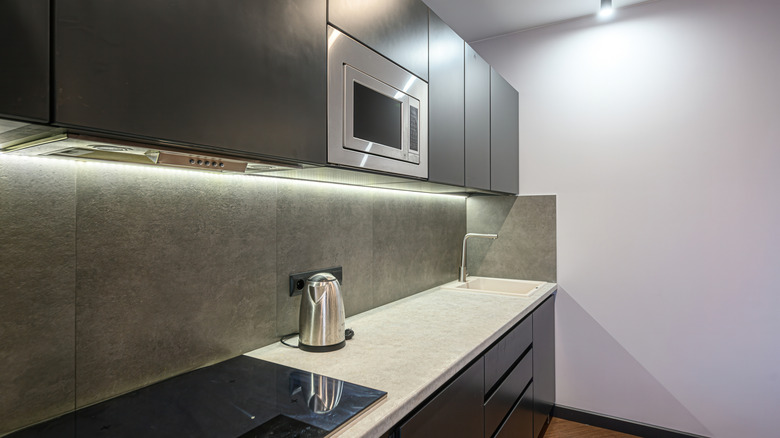 Modern kitchen with dark cabinets, stone backsplash, a stainless steel microwave, and built-in lighting.