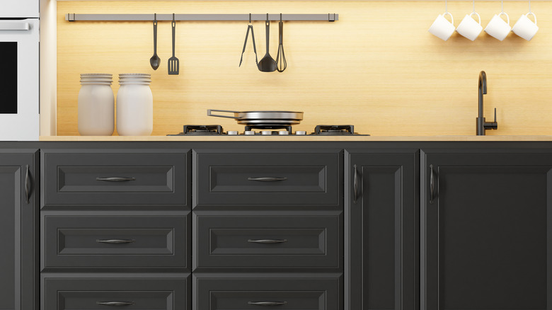 Yellow wallpaper backsplash over dark matte cabinets and stainless appliances and utensils.