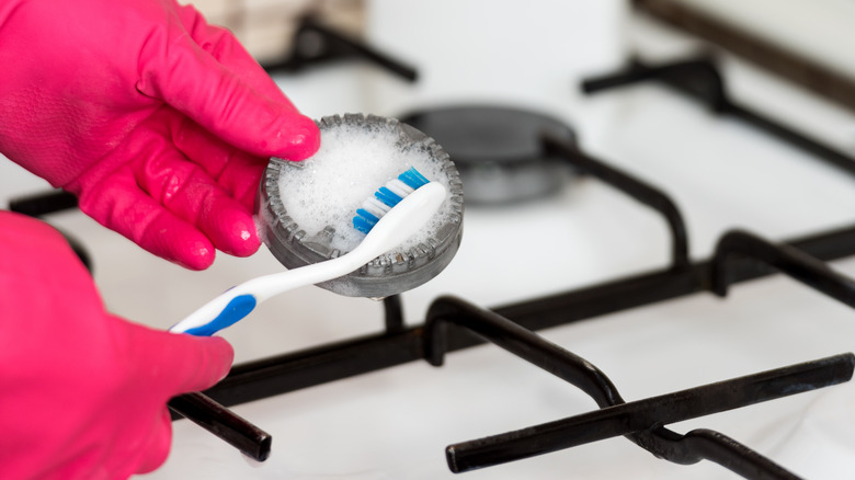 person cleaning stove with toothbrush