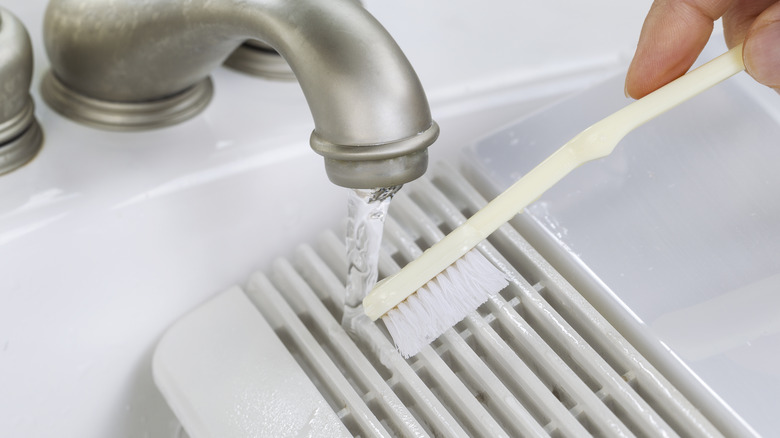 person cleaning vent grate with toothbrush
