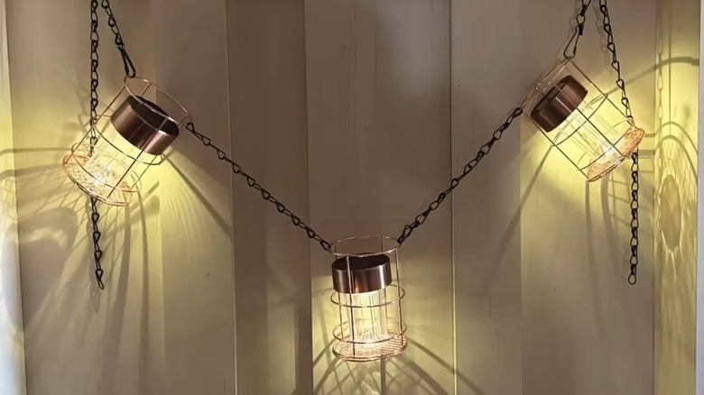 DIY solar light lanterns are strung together against white fencing.