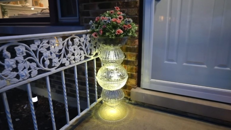 A glowing plant stand made of clear bowls and solar lights sits on a front porch.