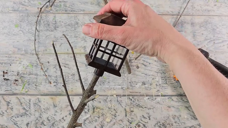 A person attaches a solar light to a natural stick.