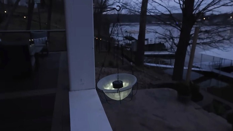 A single hanging solar light rests against a white wooden deck beam.
