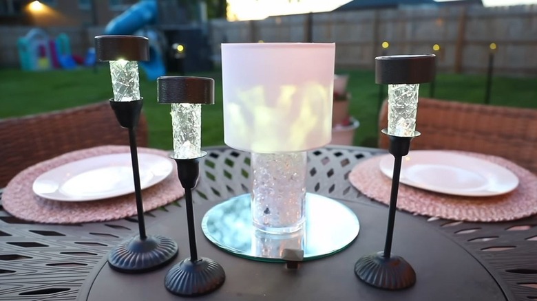 Three solar light candles sit on a patio table outdoors at dusk.