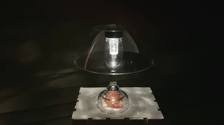 An all glass lamp sits on an outdoor table at night.