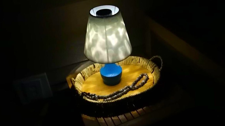 A blue lamp sits on an outdoor side table with a solar light in lieu of a lightbulb.