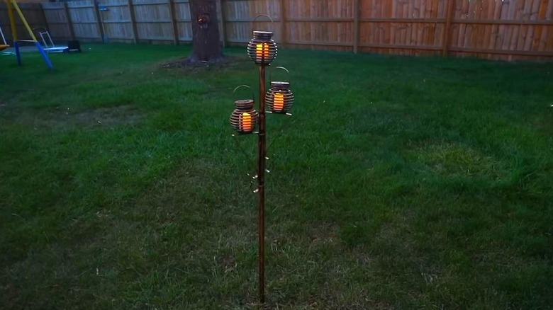 A solar light lamppost with three lanterns in a backyard.