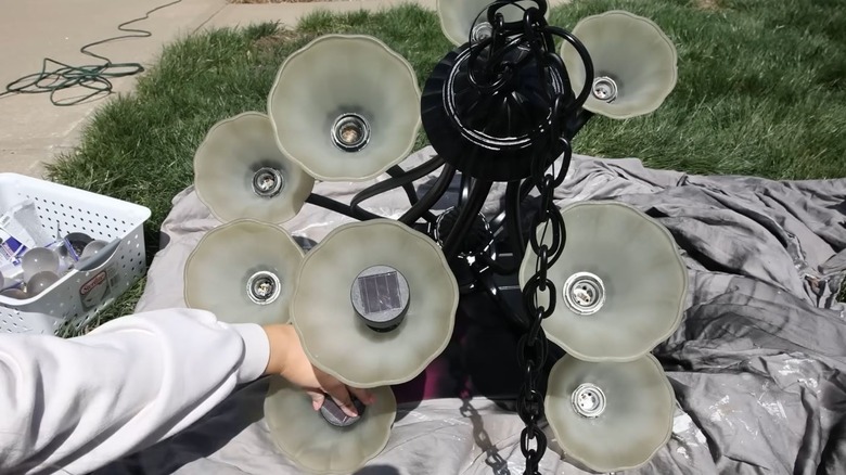 A person glues solar lights into the light sockets of an upcycled chandelier.