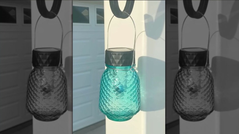 A blue hanging glass jar holds a solar light outside.