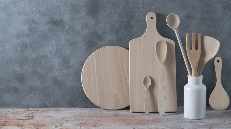 Cooking spoons in a container and resting agains cutting boards on a grey wall with a wood counter top