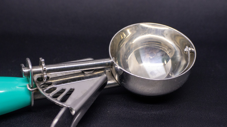 Metal icecream scoop with a teal handle on a dark surface