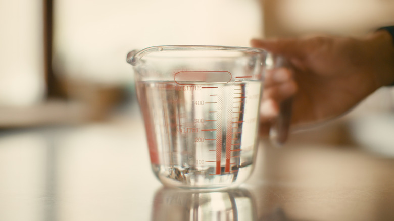 Hand placing a liquid measuring cup full of water on a counter