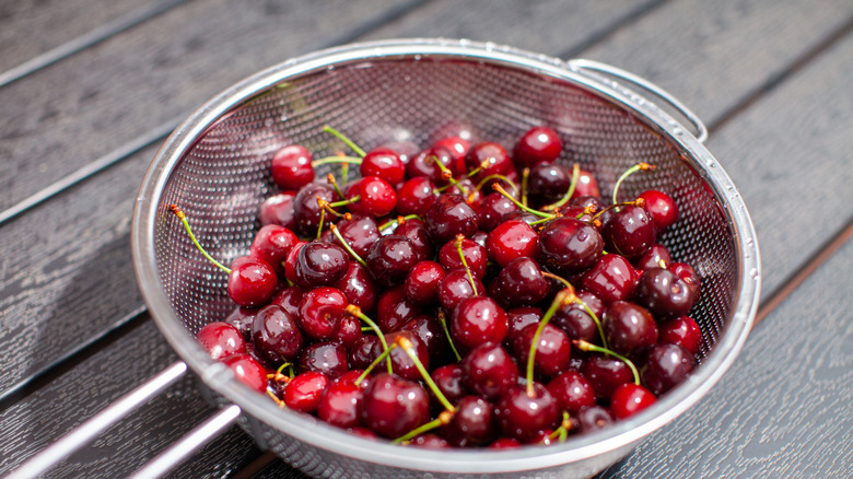 Red cherries with stems in a mesh strainer on a wood paneled surface