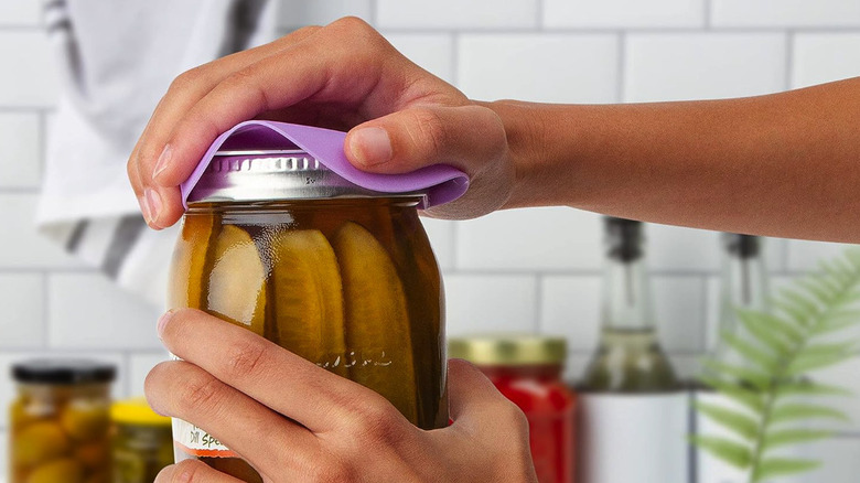 Hands using a silicon jar opener to open a pickle jar